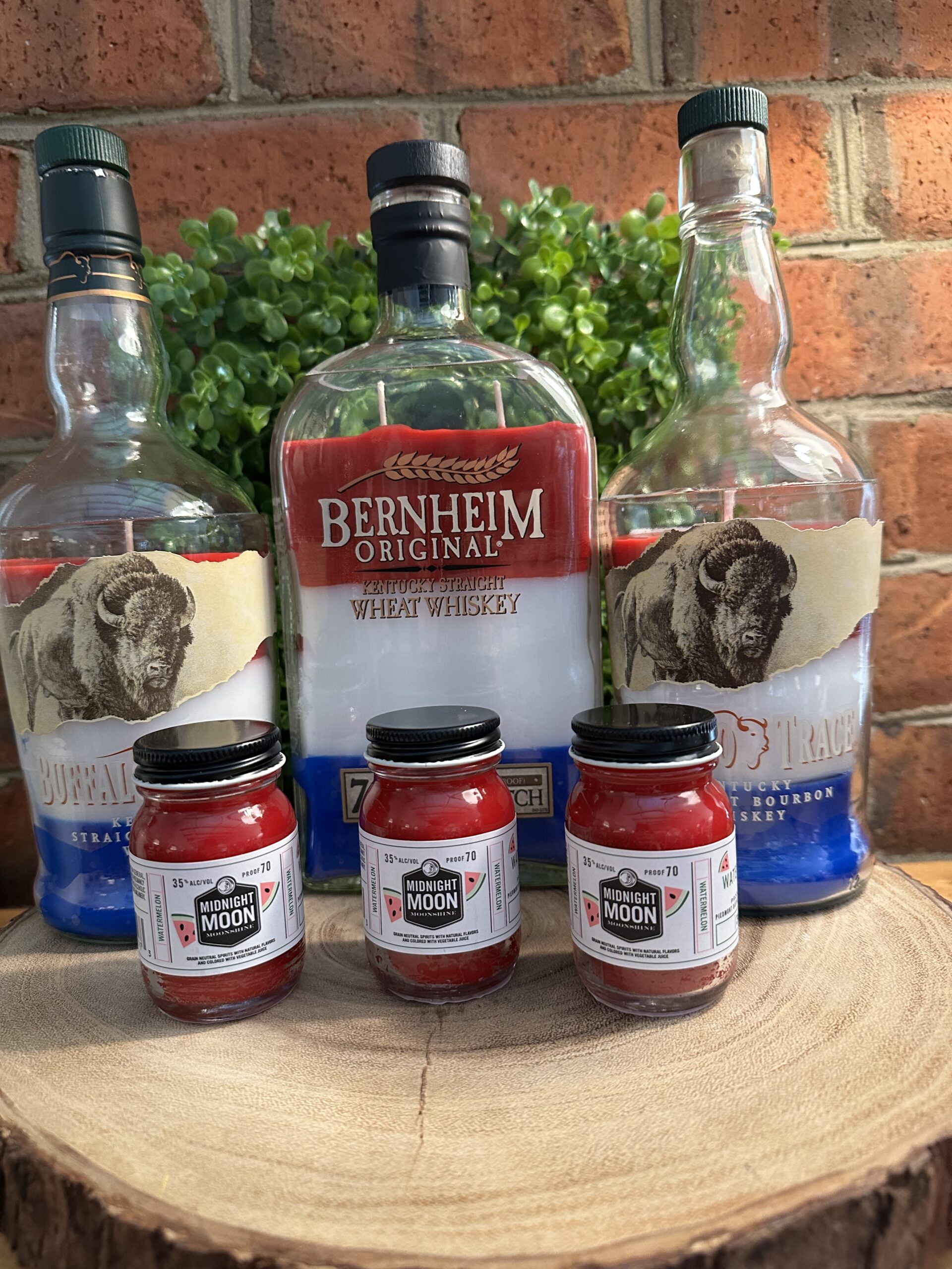 Custom bottle candles made from upcycled Buffalo Trace, Bernheim Original, and Midnight Moon moonshine bottles featuring red, white, and blue layered wax, demonstrating The Lighthouse Candle Factory's custom bottle cutting program.