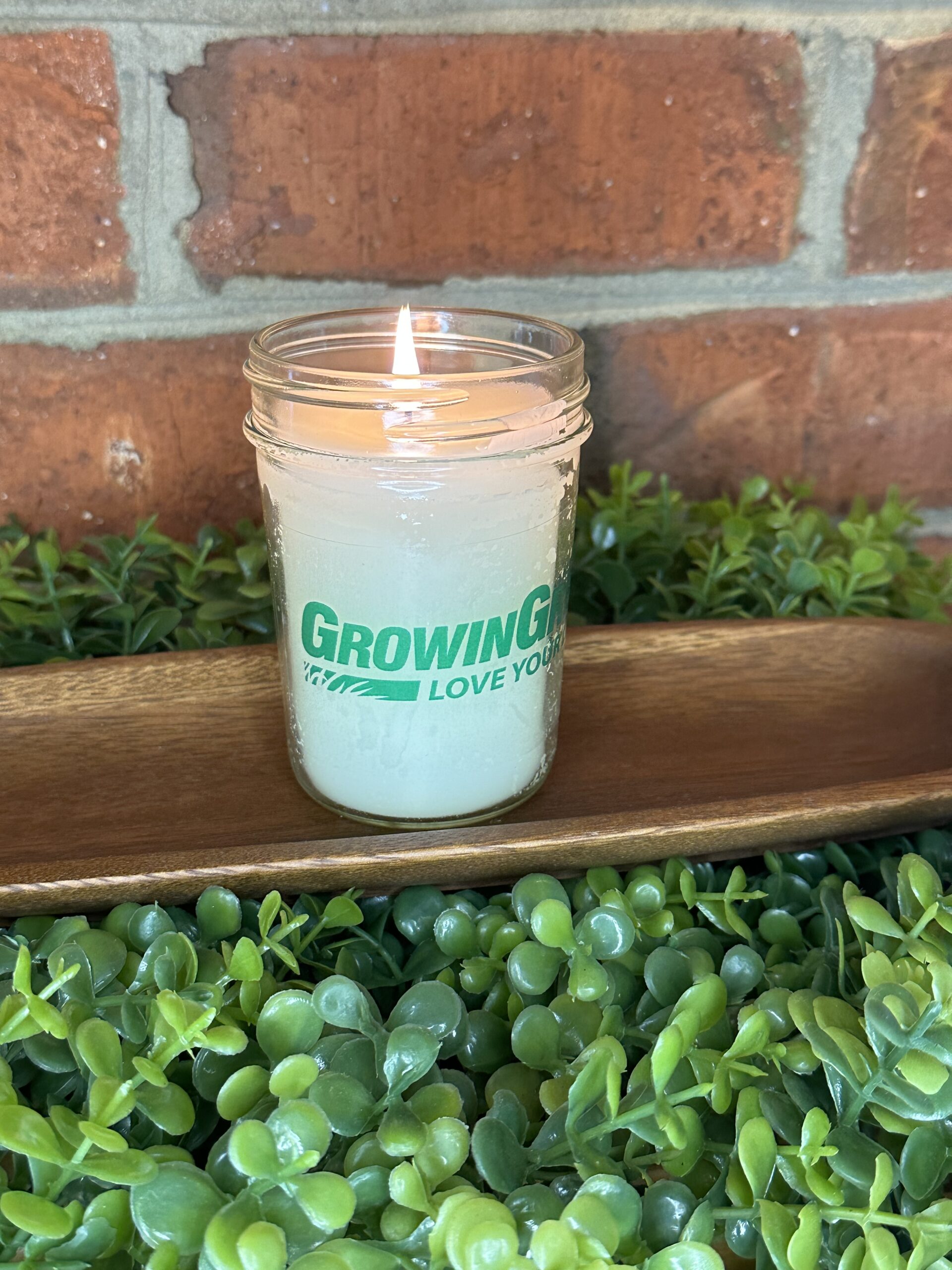 One of The Lighthouse Candle Factory's Custom Corporate Candle Gifts inside a clear glass jar with white wax featuring the GrowinGreen logo.